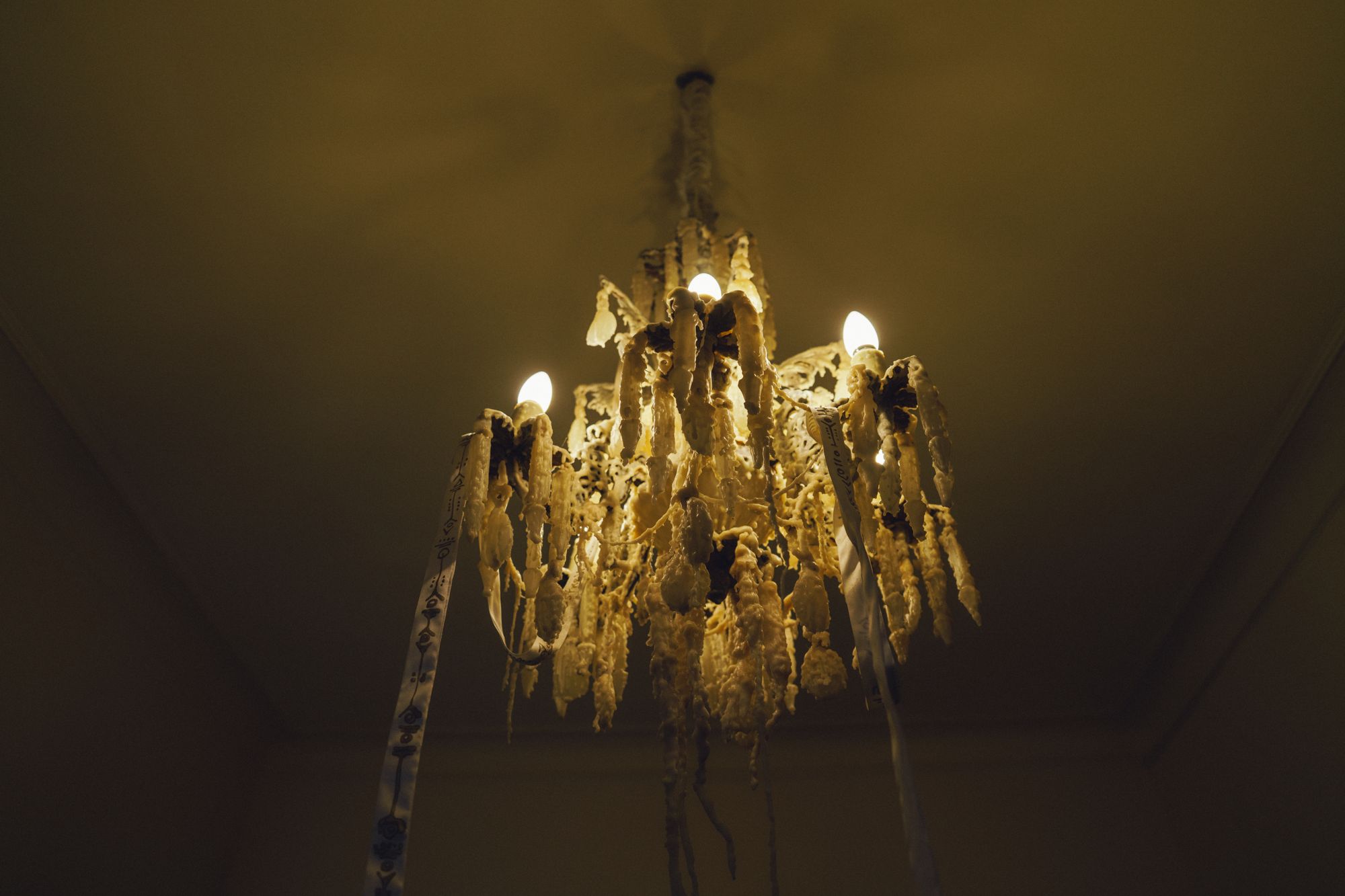 Memorias de Cera: wax-encrusted chandelier glowing in a dark room
