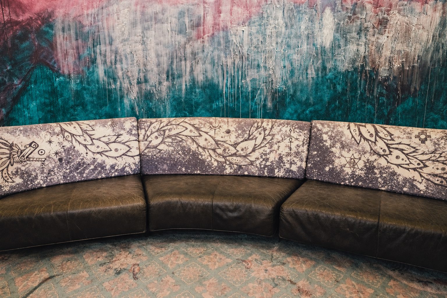 Curved leather sofa with painted symbol-covered cushions, set against a large abstract mural