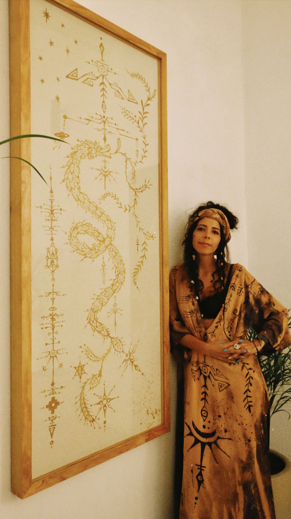 Pau standing beside a framed serpent codex in a woven garment